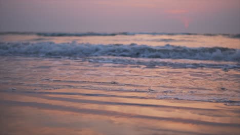 waves and sea foam on sandy beach during golden hour of sunset, static dreamy background slow motion