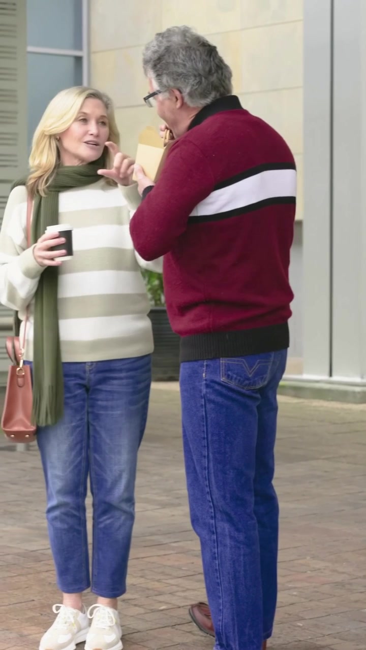 Vertical video: Opening takeout man in maroon using chopsticks talking at plaza, woman holding cup