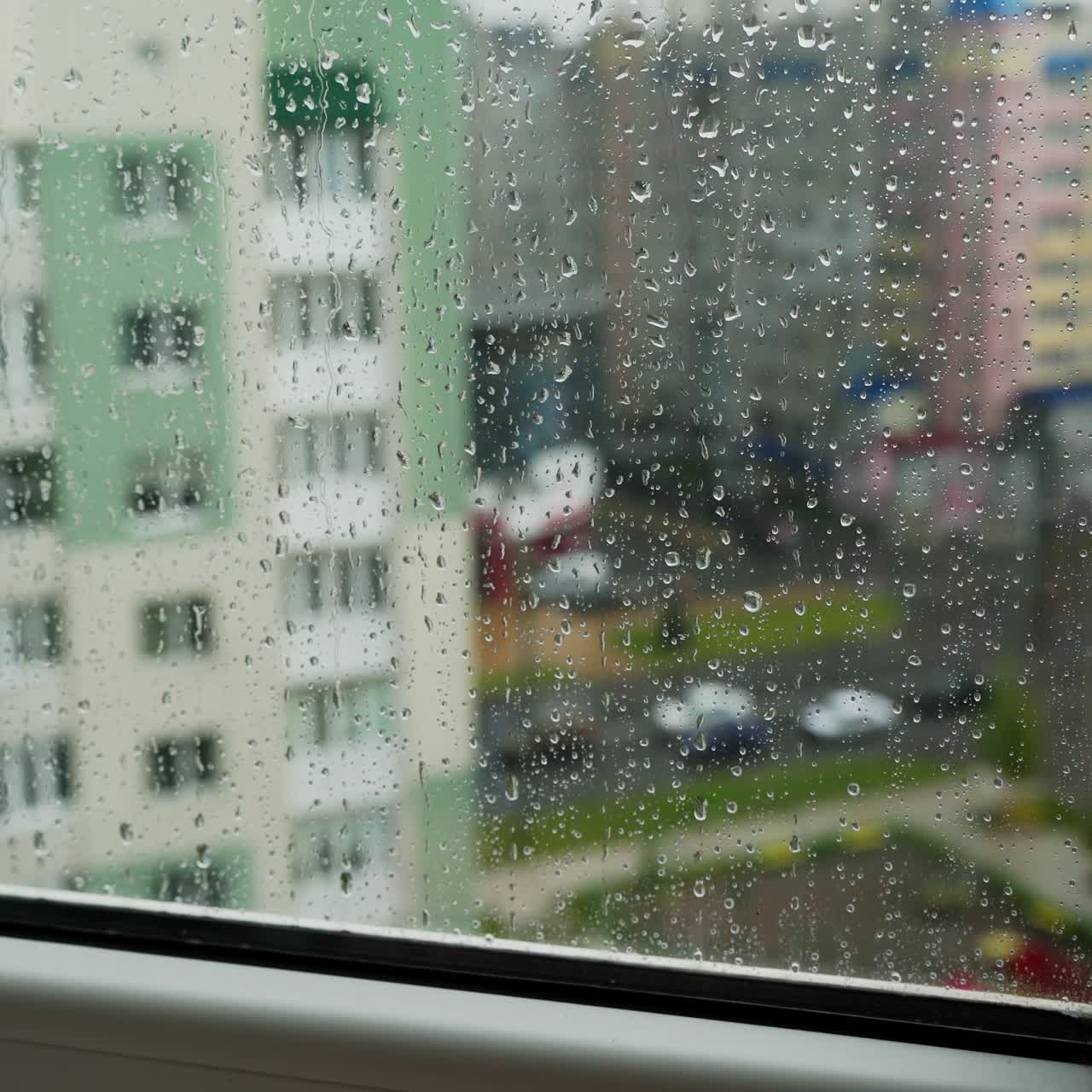 Rain drops on window glass in viewing cityscape. Drops of rain on a window pane with buildings background. Raining scenery on window.