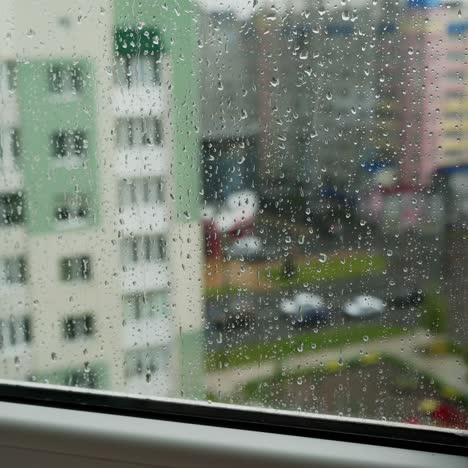 rain drops on window glass in viewing cityscape. drops of rain on a window pane with buildings background. raining scenery on window.