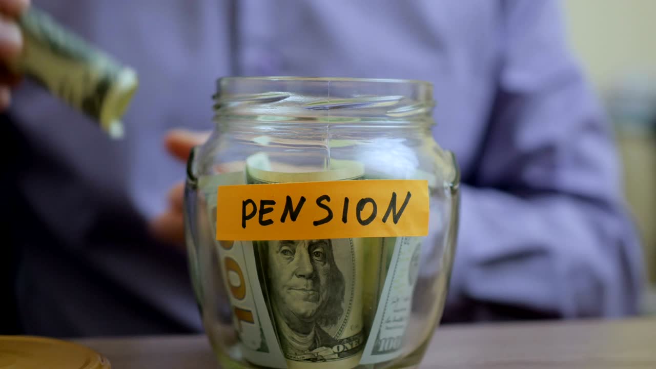 hombre caucásico poniendo un frasco de vidrio puesto en una mesa de cajón con sus ahorros para la futura pensión
