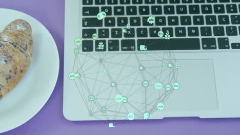 animación de globo de iconos digitales girando contra el primer plano de croissant en un plato y portátil