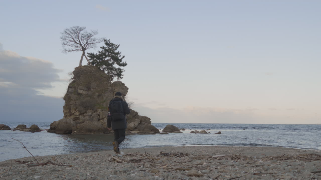 Young man walking towards a sacred rock over the ocean, Amaharashi Coast, Japan