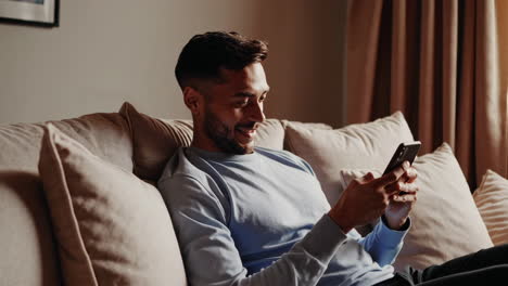 man relaxing and using his phone on a couch at home