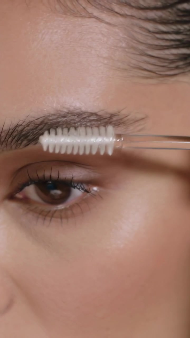 Vertical video: Entering spoolie grooming left brow on woman at vanity, shaping brow, copy space