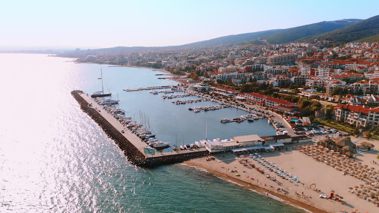 Flying closer to the sandy beach located near the modern yacht club. Aerial perspective on the resort city Sveti Vlas in Bulgaria