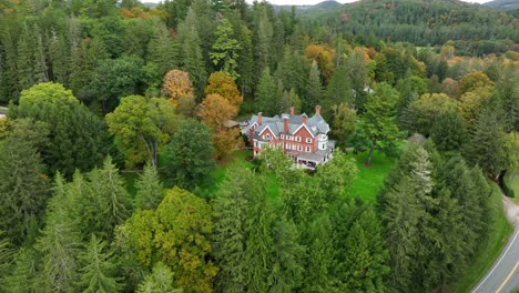 Toma-Aérea-Rotacional-De-Drones-De-Una-Mansión-De-Ladrillo-Entre-Bosques-De-Pinos-Y-Hojas-De-Otoño-Cambiantes