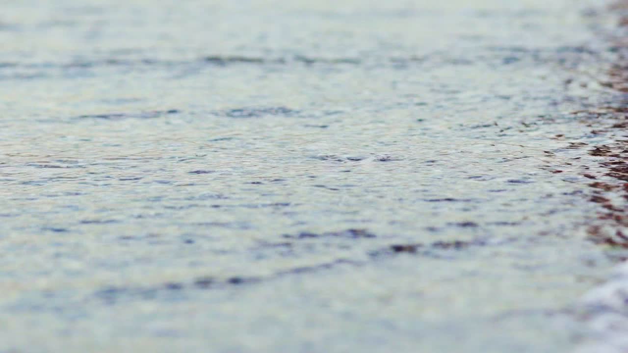 Surface of water sea ocean wave with white foam close-up on a beach. Beautiful waves of water crashing onto the small rocks and shore. Summer vacation holiday at the sea.