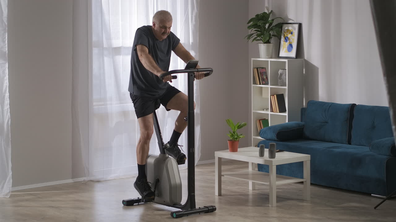 perder peso y entrenar el sistema cardiovascular usando la bicicleta estacionaria en casa hombre adulto está haciendo ejercicios deportivos en la bicicleta de ejercicio en la sala de estar