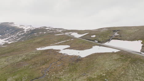 Drone-following-a-campervan-traveling-on-Bjorgavegen-snow-capped-mountain-pass