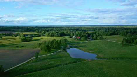 Paisaje-Escénico-Con-Un-Lago-Y-árboles-Forestales-Verdes-Que-Cubren-El-Vasto-Campo-En-Letonia-Desde-Un-Disparo-De-Drone