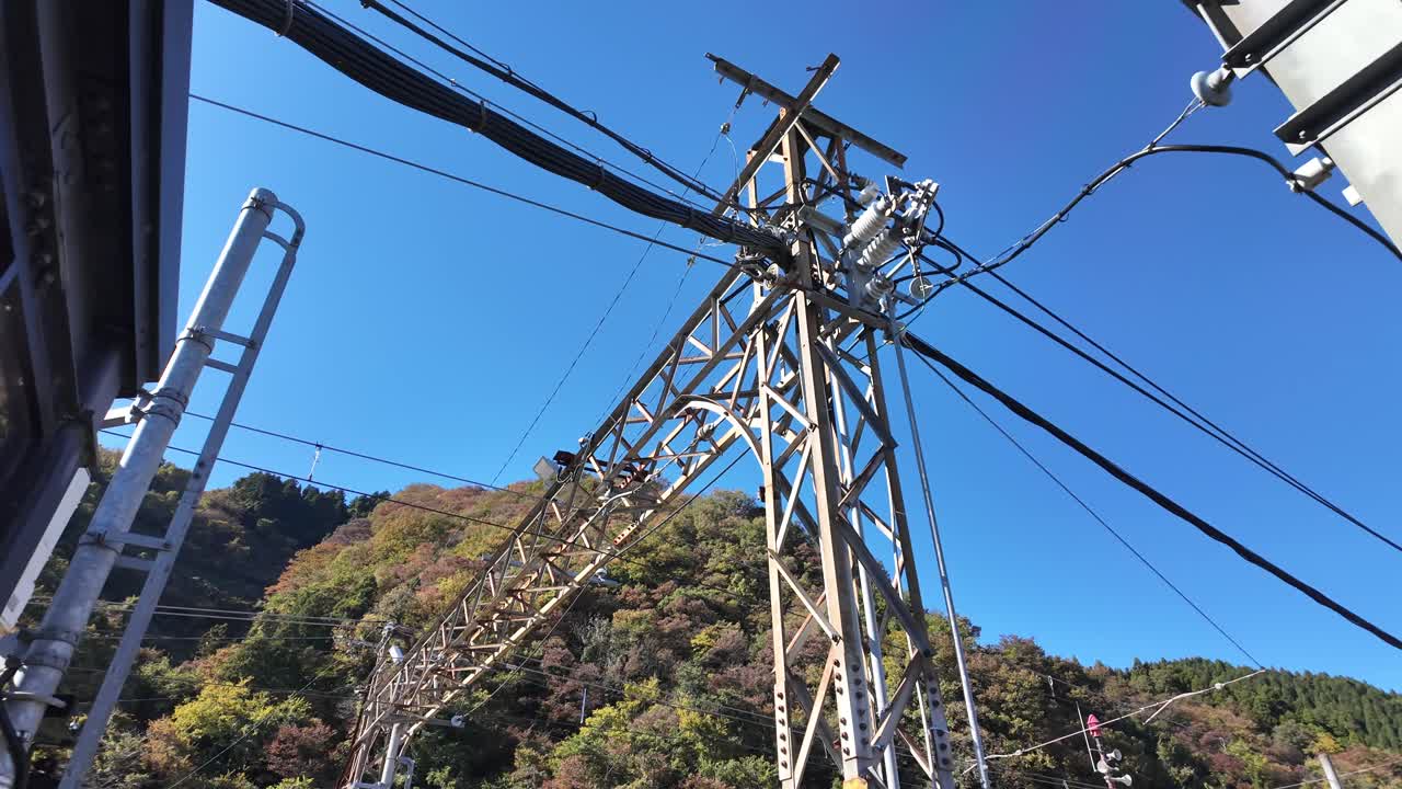 Railway gantry with wires against blue sky and mountains in autumn surroundings.