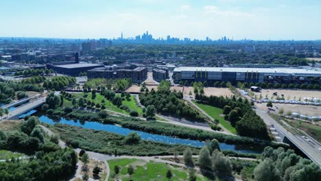 Aerial-descending-view-Stratford-park-and-gardens-with-iconic-London-skyscraper-cityscape-towers-on-blue-sky-horizon