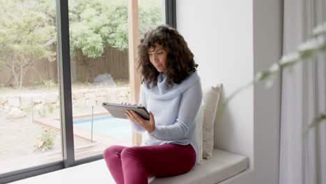 feliz mujer caucásica madura sentada en la ventana y usando la tableta en casa, cámara lenta