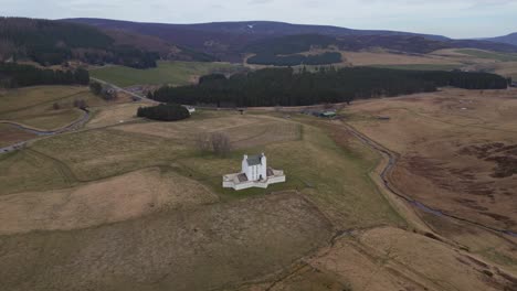 flight over the beautiful scottish highlands towards a charming white church and view of the lush forest and captivating landscapes that unfold beyond the church