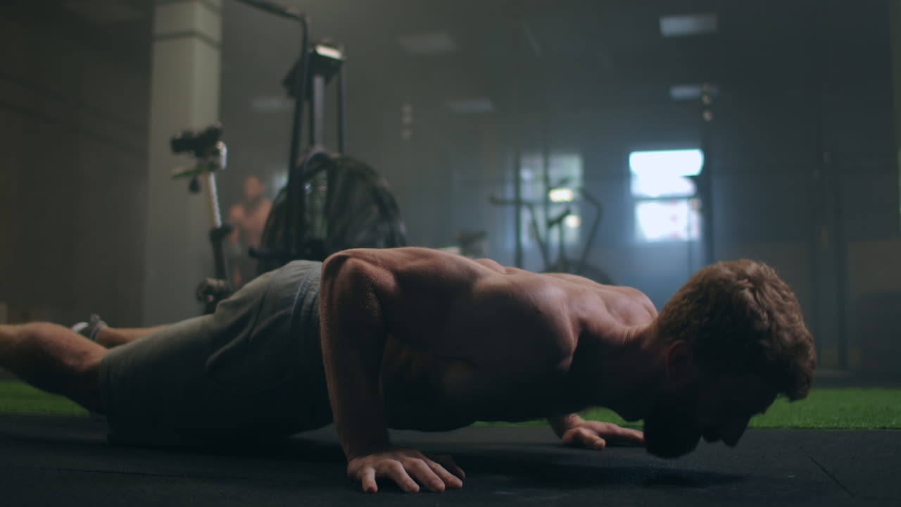 un hombre atlético fuerte y en forma con camiseta deportiva y pantalones cortos está haciendo ejercicios de empuje en un gimnasio industrial de estilo loft con carteles motivacionales. es parte de su entrenamiento de fitness cruzado.