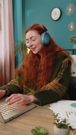 redhead woman listening music through wireless headphones relaxing taking a break laptop on table
