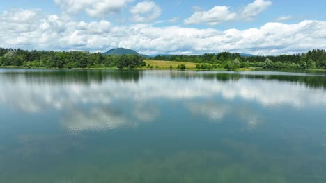 Drones-Aéreos-Vuelan-Cerca-Del-Prístino-Paisaje-Del-Lago-Žovnek-En-Eslovenia,-Campos-Verdes,-Paisaje-Nublado-De-Verano,-Nubes-Sobre-El-Agua,-Braslovče