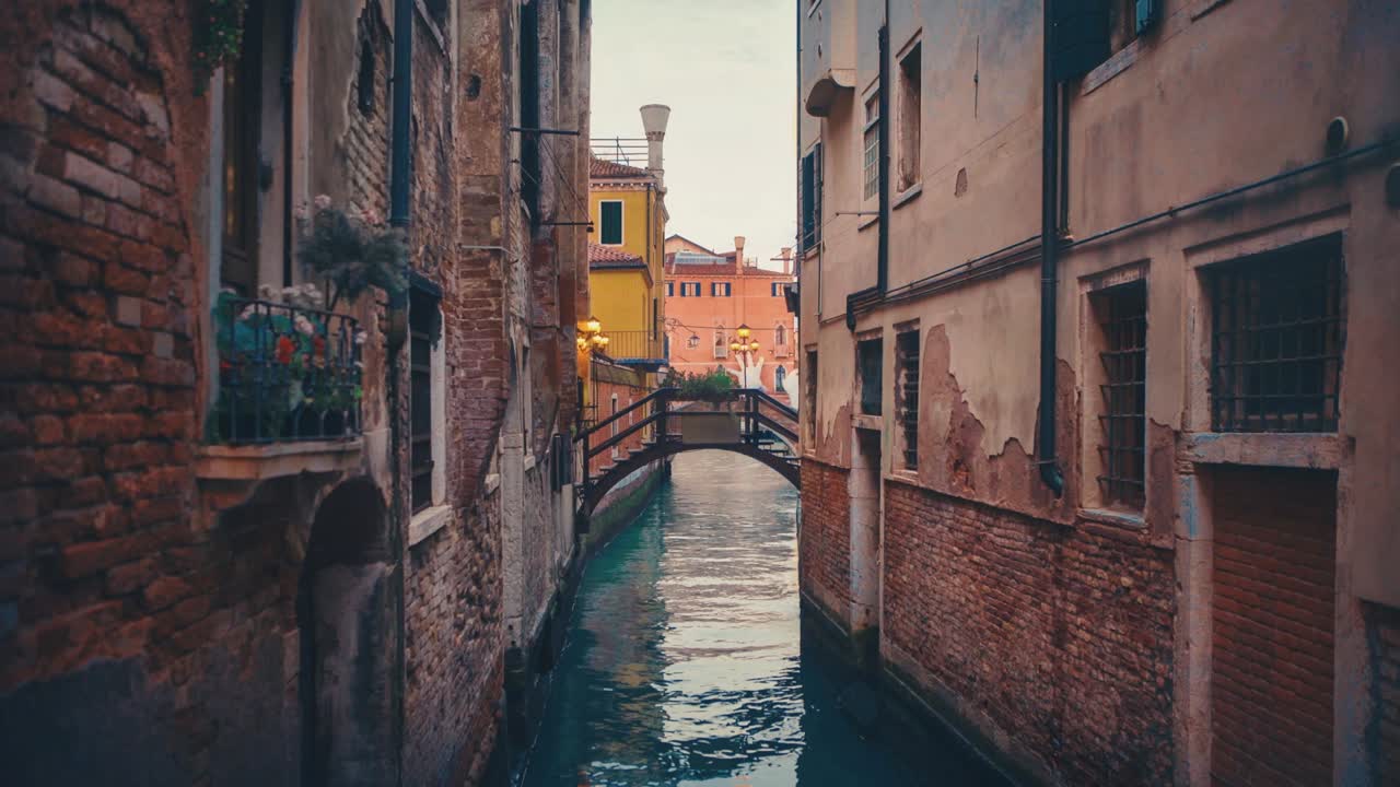Seamless video loop / Cinemagraph of a Venetian canal with a bridge among the old medieval houses in the old town city center of famous UNESCO Heritage Site Venice in Italy with clear blue water and ships and boats in the tourist vacation location.