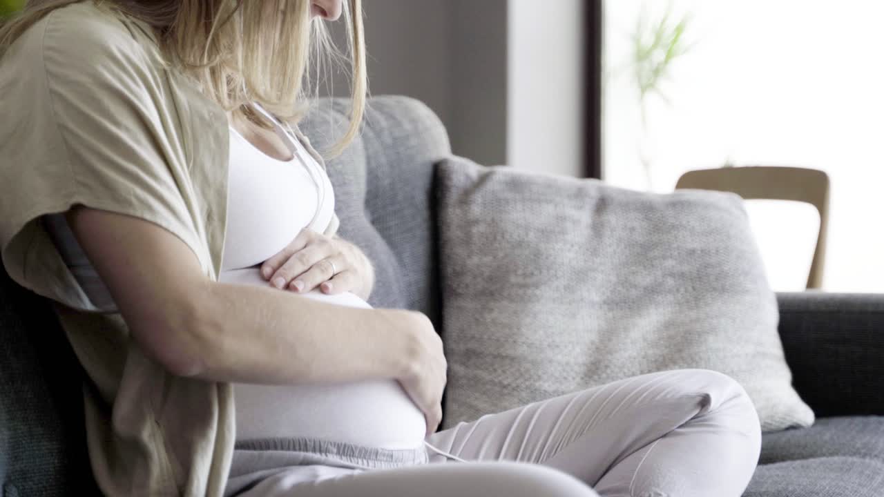 침착 한 임신 한 여자 가 배 를 마사지 하고 음악 을 듣고 있다