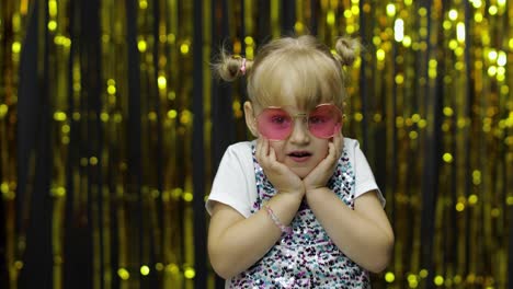 child dancing, show amazement, fooling around, smiling. girl posing on background with foil curtain