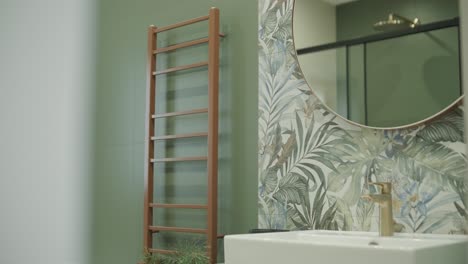 a stylish bathroom corner featuring a modern white sink with a brass faucet, set against a lush botanical wallpaper and a wooden towel ladder, blending functionality with nature-inspired aesthetics