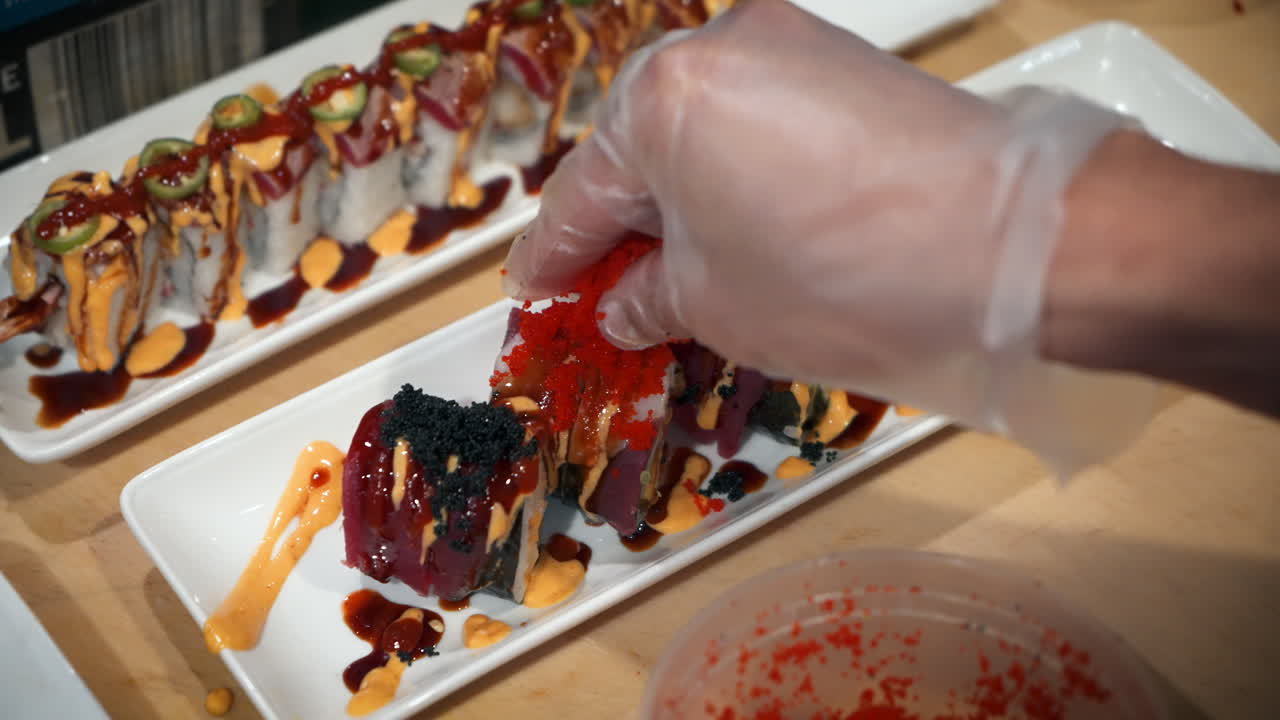 Sushi chef garnishes prepared roll with red masago, slow motion close up 4K