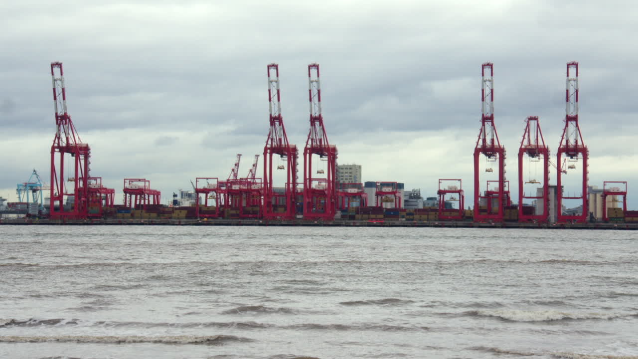 Wide shot of Liverpool container terminal and Cranes next to the river Mersey on a cloudy day at New Brighton beach