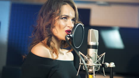 young brunette woman recording a song or album in a professional studio. beautiful girl singing emotionally near the modern microphone in sound room.