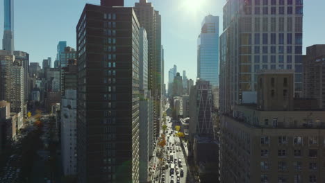 Forwards-fly-above-street-crossing-and-between-modern-high-rise-buildings-in-city-on-sunny-day.-Manhattan,-New-York-City,-USA