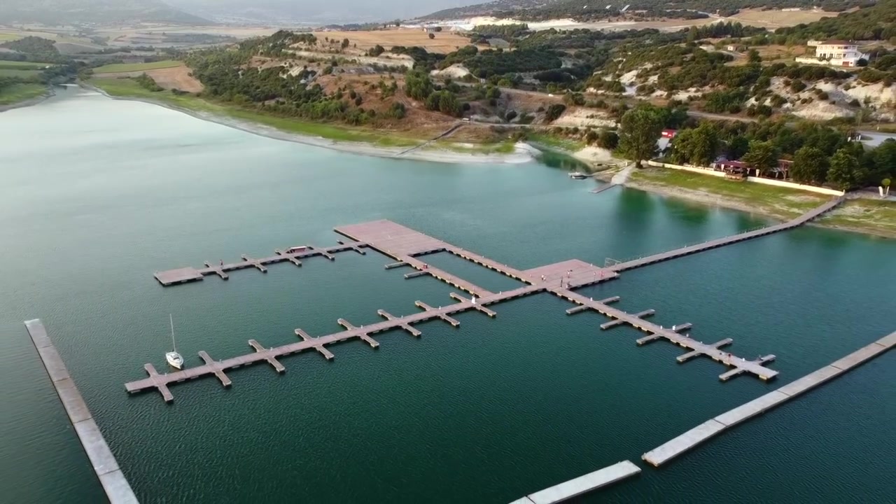 Ripresa panoramica dall'alto con drone che cattura le acque scenografiche del bacino idrico del lago Polyfytos e il molo del Nautical Club vicino a Servia