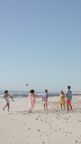 Vertical video: Group of friends playing soccer on beach, enjoying sunny day together