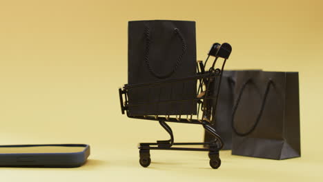 video de teléfono inteligente, bolsas de compras y carrito con espacio de copia sobre fondo amarillo