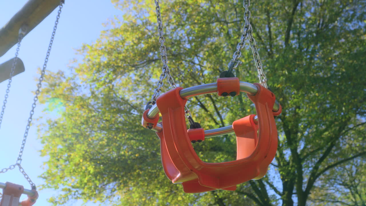 Empty child's swing moving slowly in English autumn sunshine