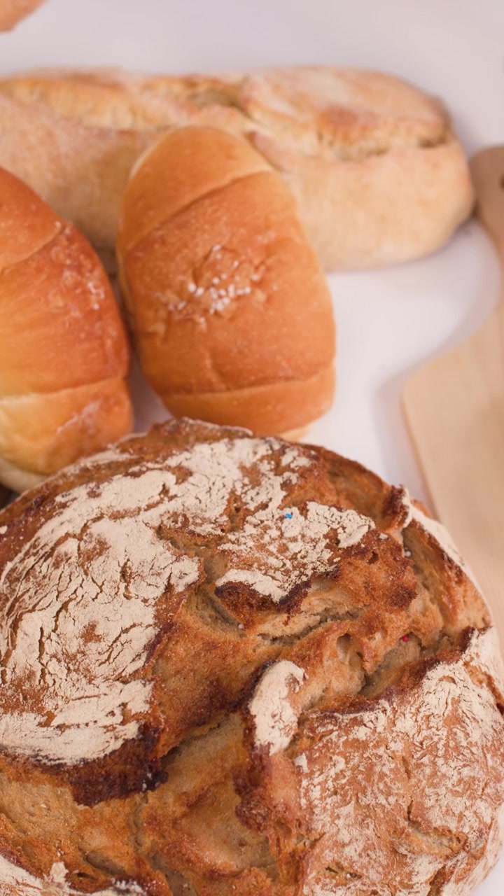 Close-up shot of hands slicing a crusty baguette on a wooden board amidst various breads.