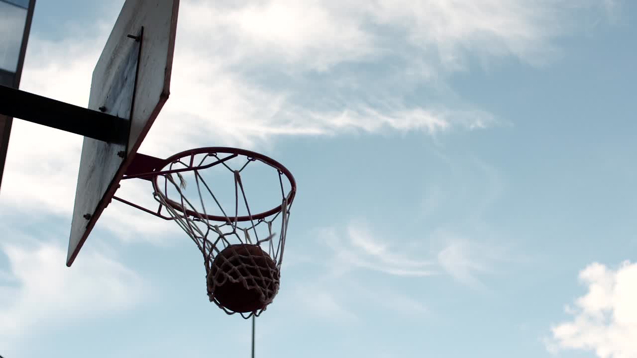 Dark skinned man dunking a basketball against a blue sky.