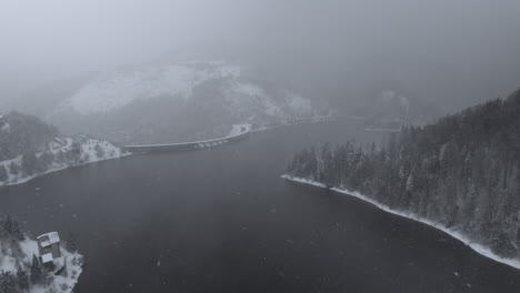 Vista-Aérea-De-Un-Lago-Y-Una-Presa-Rodeada-Por-Una-Cautivadora-Mezcla-De-Niebla-Y-Nieve,-Bosque-De-Montaña,-En-La-Presa-Dragan-De-Transilvania,-Rumania