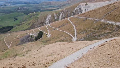 three people on curved road leading up a dry, bushy mountainside