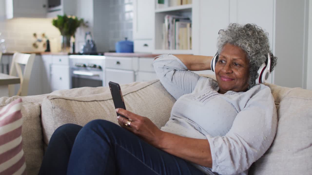 Anziana donna afroamericana con le cuffie in videochiamata sullo smartphone a casa.