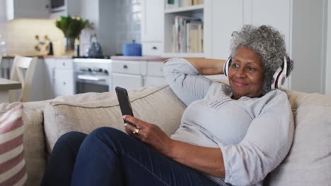 senior african american woman wearing headphones having a video call on smartphone at home