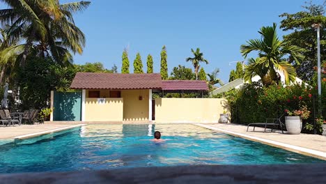 Middle-aged-white-man-swimming-away-from-camera,-breast-stroke,-gentle,-relaxing-exercise-in-outdoor-swimming-pool-on-a-blue-sky-hot-and-sunny-day-whilst-on-vacation-holiday