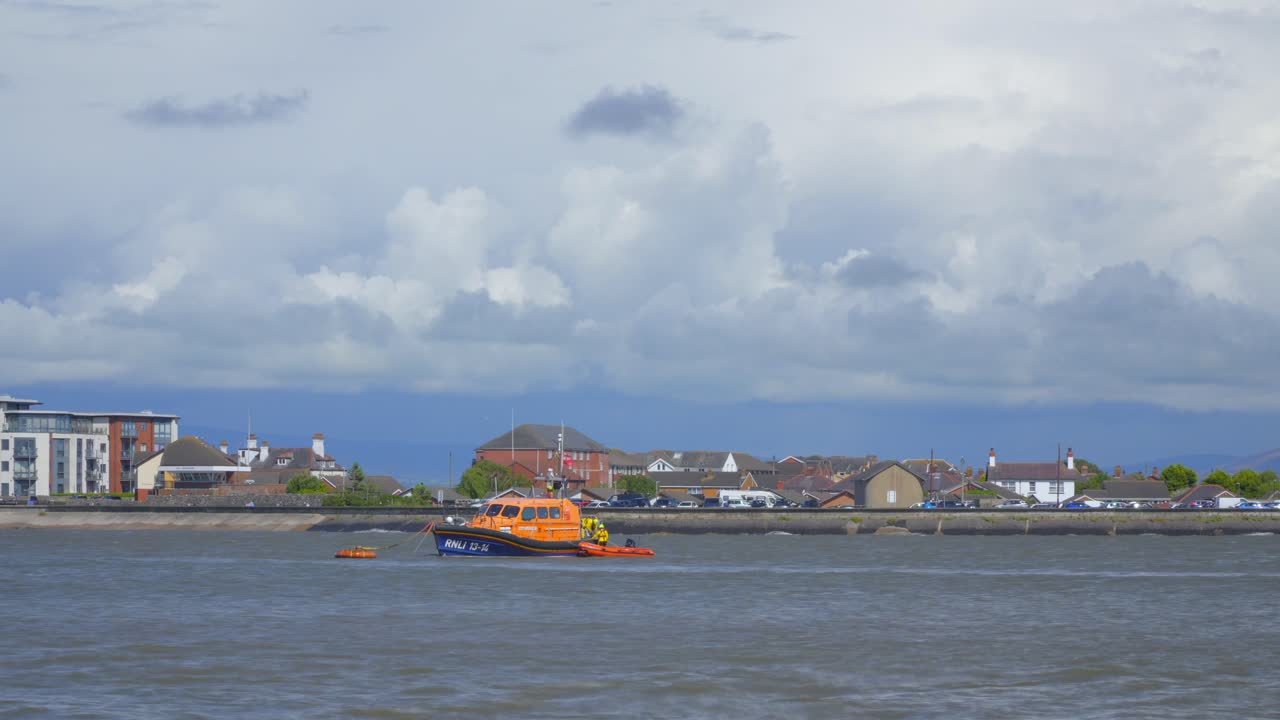 구명 보트 승무원 들 이 구명 보트 를 타고 나서 구름 이 가득 한 하늘 을 가로지르는 요트 와 제트 스키 와 함께 스크린 을 떠난다