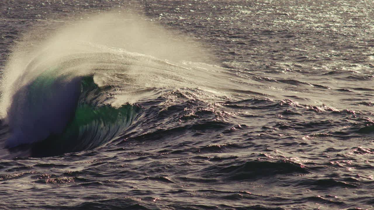 Moody dusk wave rises in shadowy sea, light edges catching curve and foamy texture below