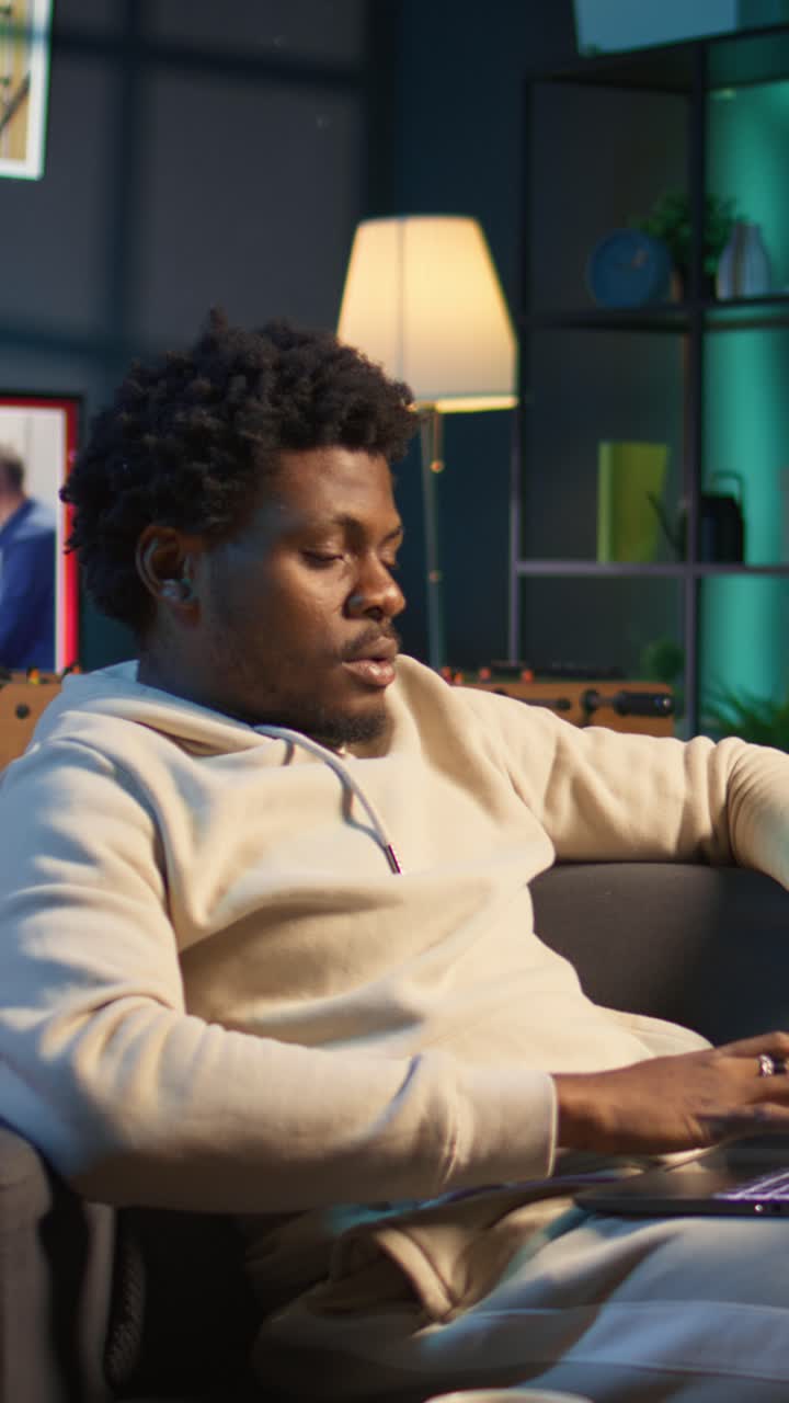 Ung afroamerikansk mann slapper av på sofaen med laptop