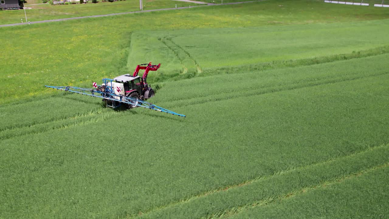 Farm worker drives through green field leaving tracks as it goes, aerial