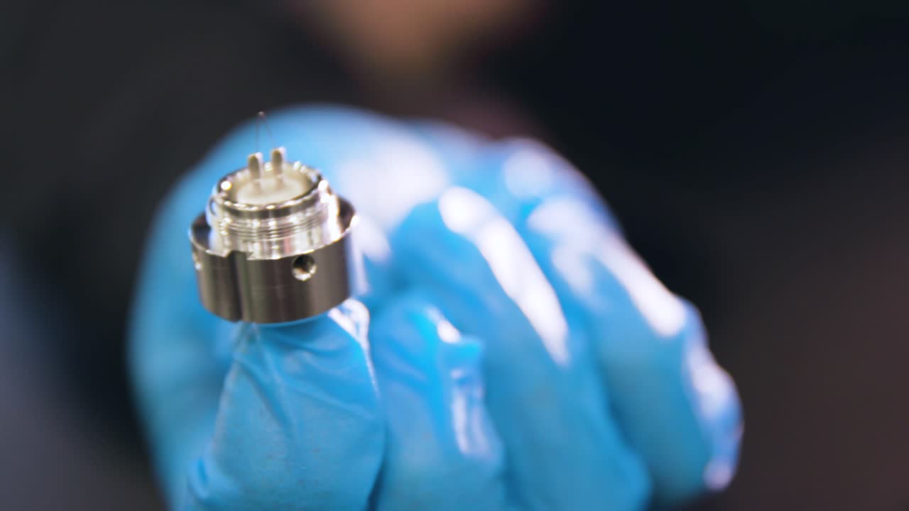 Close-up of a small metal electronic component held in blue gloves