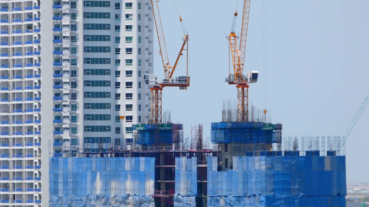 都市の建設現場でタワークレーンが稼働し、継続的な建設の進捗と現代都市の発展を捉えたタイムラプス映像。