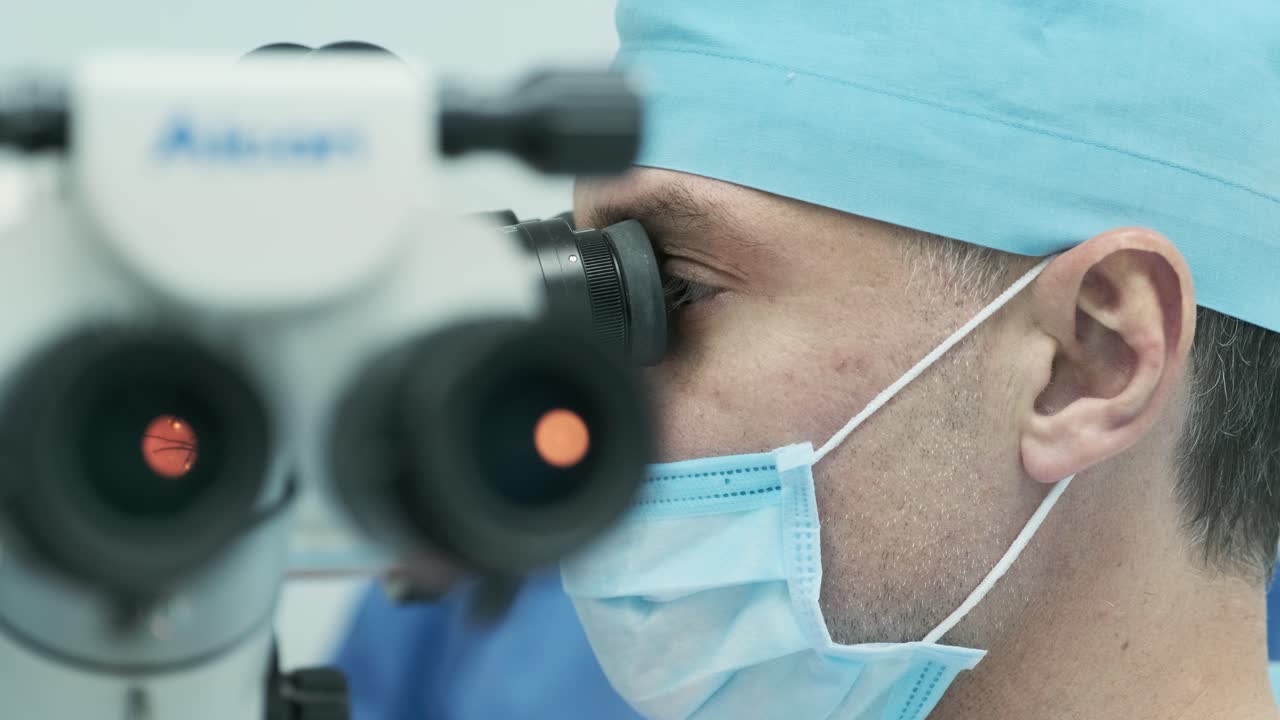 Surgeon looking into the microscope at the eye of female patient at the operating room. Doctor using microscope during eye surgery process, treatment of cataract and diopter correction.