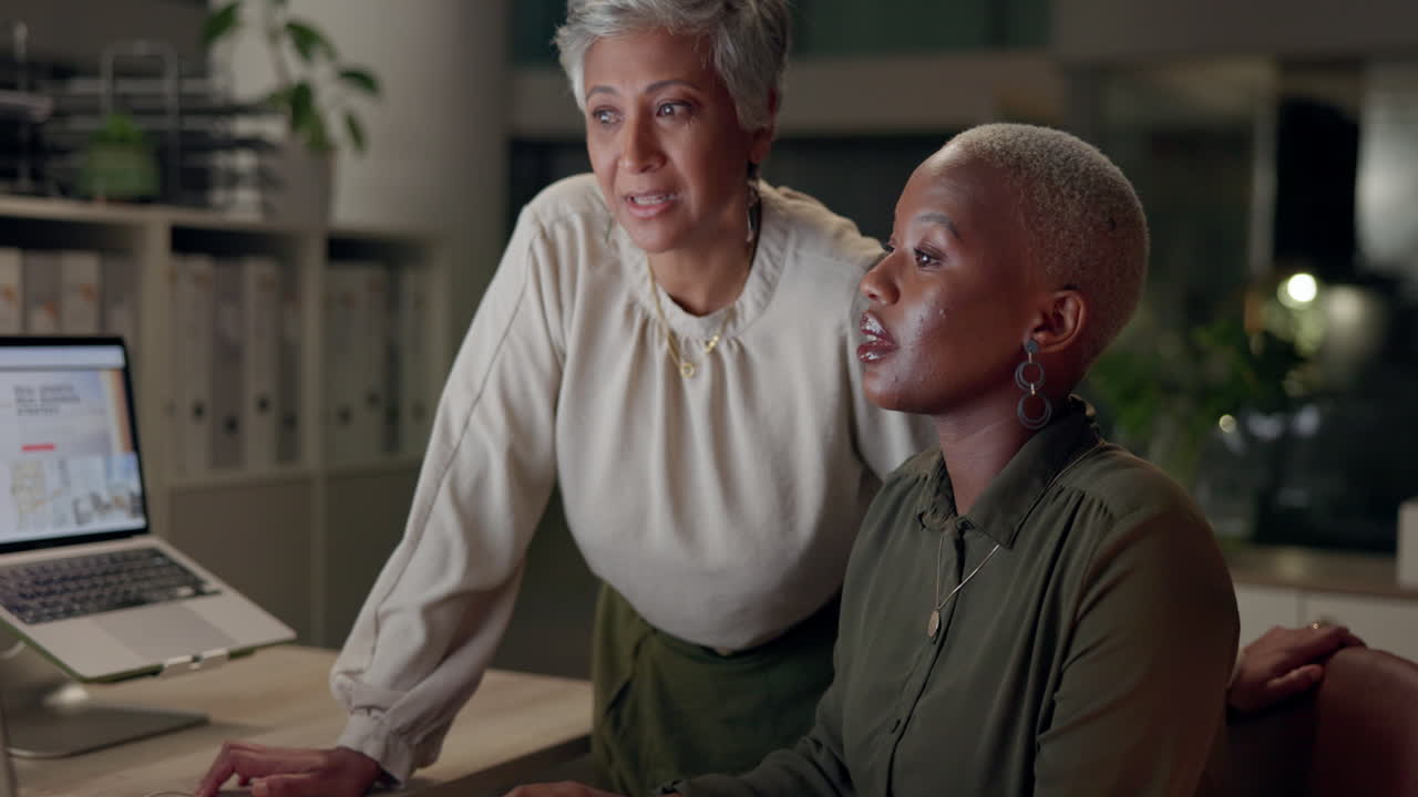 Two women collaborating in an office using a laptop