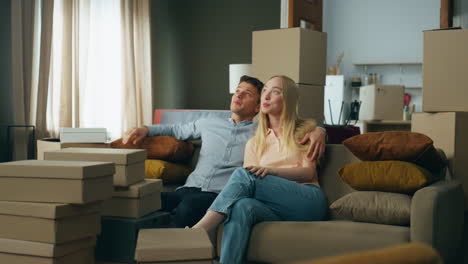 Pareja-Joven-Sentada-En-Un-Sofá-Inspeccionando-La-Sala-De-Estar-Después-De-Mudarse-A-Una-Casa-Nueva.